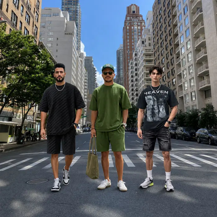 Three models wearing oversized streetwear outfits including graphic tees, matching set, and relaxed fit clothing in an urban city setting.