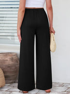 Close up of the secure flat lock stitching and flexible elastic waistband on CLOTHRA wide leg streetwear trousers. in color Black Back side view