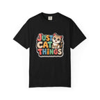 A black short-sleeve crewneck t-shirt featuring a colorful graphic on the chest that reads 'JUST CAT THINGS' in a retro, multi-colored bubble font next to a cute cartoon kitten.