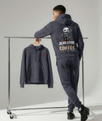 A model wearing a dark gray hoodie and matching sweatpants stands beside a clothing rack in a studio. The hoodie has a large back graphic with a skeleton and the text 'DEAD INSIDE COFFEE', and the matching pants are shown hanging on the rack.